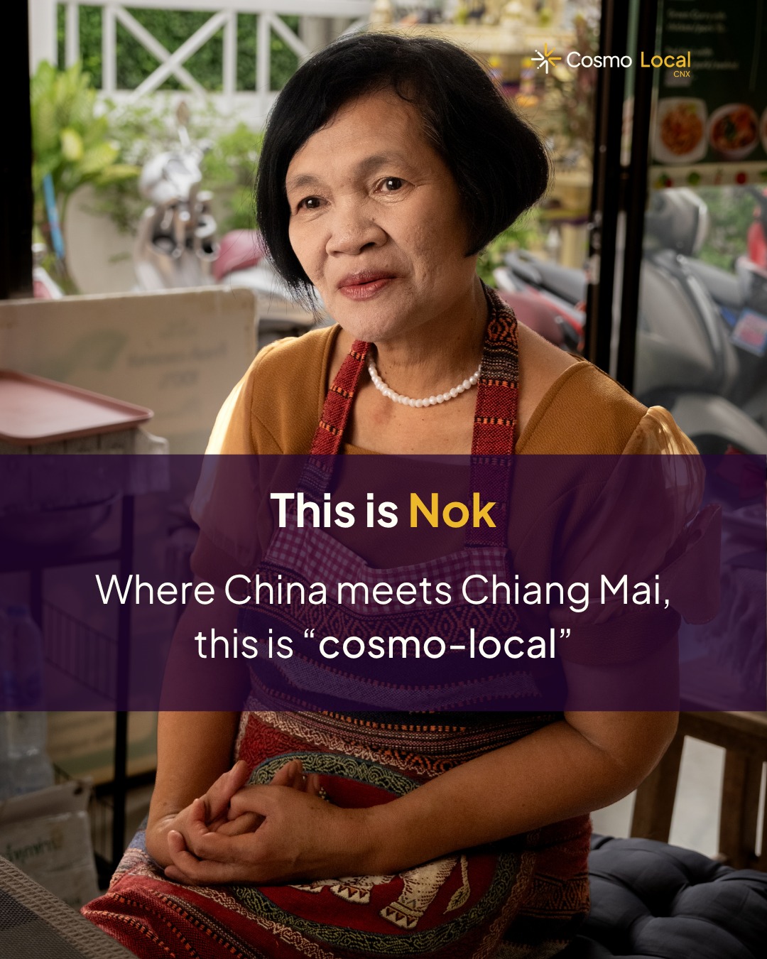 Portrait of Phi Nok in a mustard blouse, pearl necklace and woven apron, seated in her kitchen in Wat Ket, with the caption This is Nok